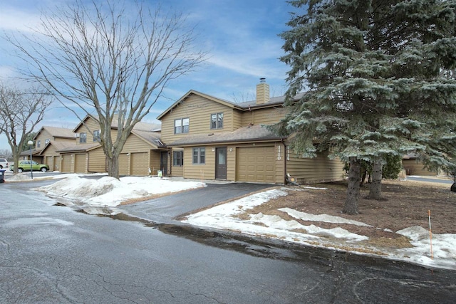 view of front facade featuring a garage, a chimney, and aphalt driveway