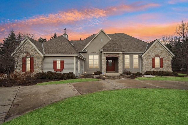 french provincial home featuring stone siding, a shingled roof, and a lawn