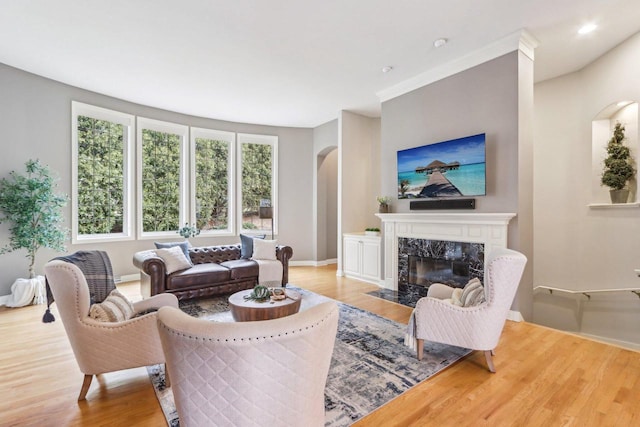 living area featuring arched walkways, recessed lighting, a premium fireplace, light wood-type flooring, and baseboards