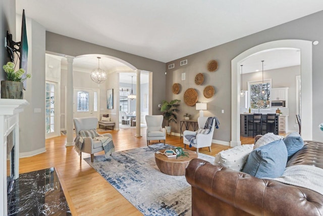 living area featuring arched walkways, a notable chandelier, decorative columns, light wood finished floors, and a fireplace with flush hearth