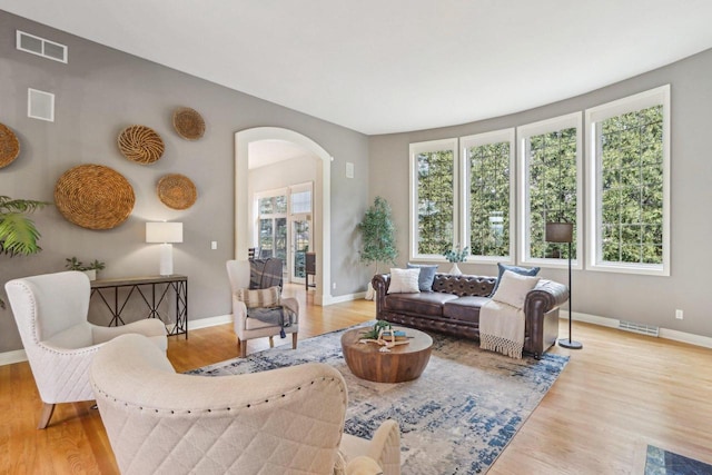 living area with baseboards, visible vents, arched walkways, and wood finished floors