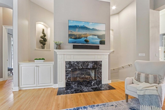 living area featuring arched walkways, wood finished floors, a high end fireplace, and baseboards