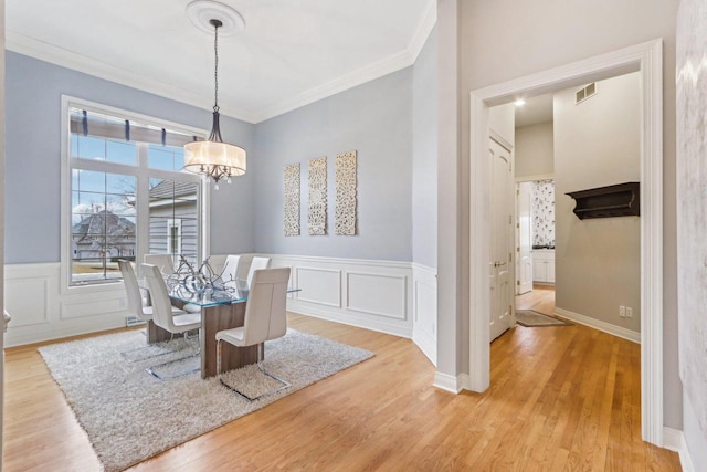 dining area with ornamental molding, light wood-type flooring, visible vents, and an inviting chandelier