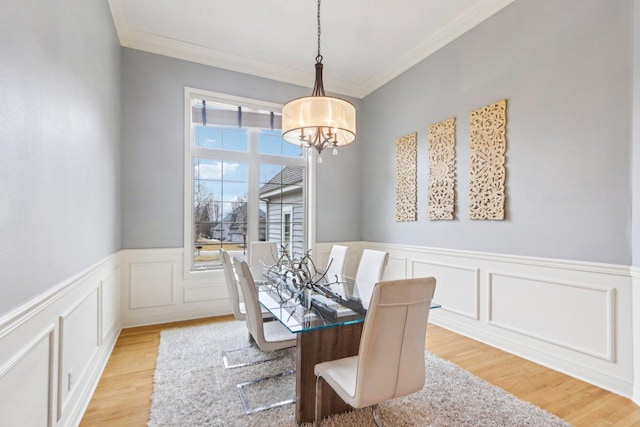 dining space featuring ornamental molding, light wood-type flooring, wainscoting, and a notable chandelier