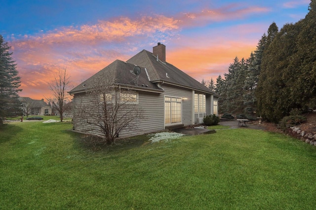 back of property at dusk featuring a chimney, a lawn, and a patio