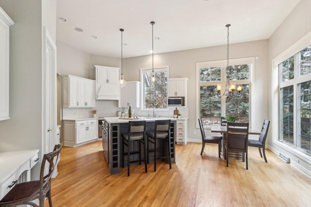 kitchen featuring a notable chandelier, stainless steel microwave, white cabinetry, premium range hood, and a kitchen bar