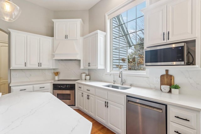 kitchen featuring white cabinets, custom range hood, stainless steel appliances, and a sink