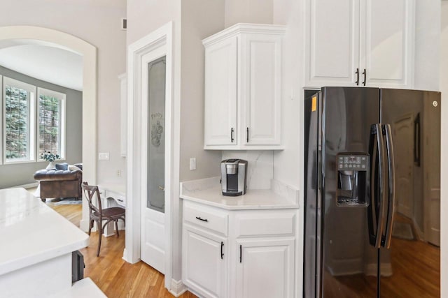 kitchen featuring white cabinetry, arched walkways, light countertops, and black fridge