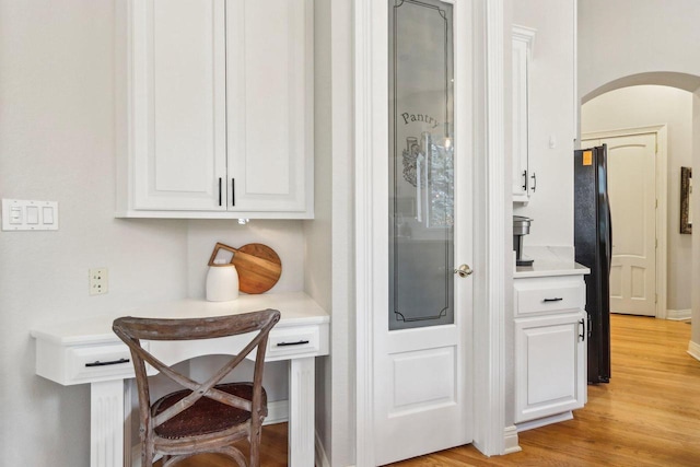 bar featuring light wood-type flooring, arched walkways, freestanding refrigerator, and baseboards