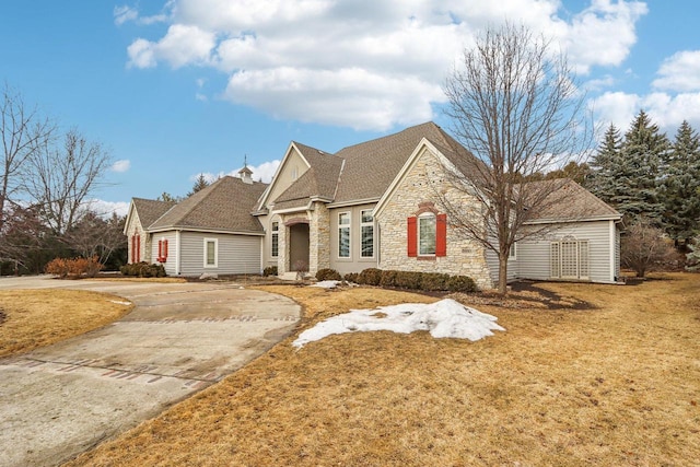 french country home with a front yard, stone siding, and concrete driveway