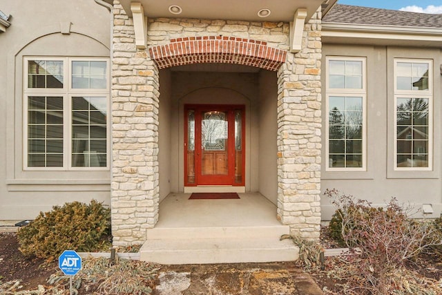 view of exterior entry with a shingled roof and stucco siding