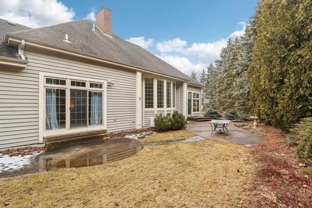 back of house featuring a yard, a patio, a chimney, a shingled roof, and entry steps