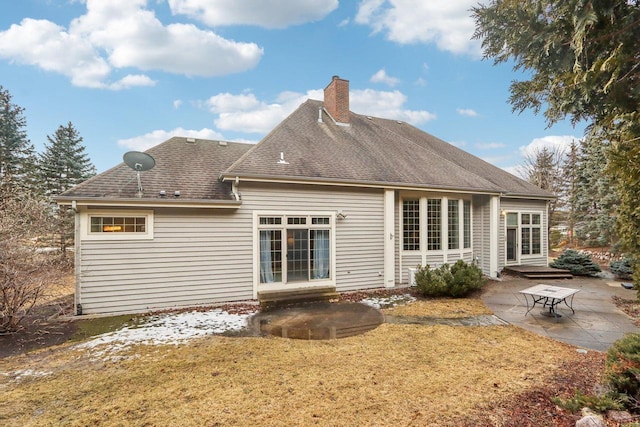 rear view of house featuring entry steps, a shingled roof, a lawn, a patio, and a chimney