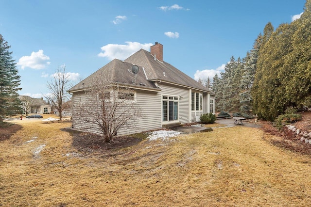 rear view of property featuring a patio area, roof with shingles, a chimney, and a yard