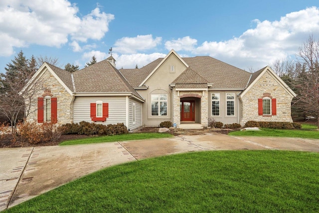 french country style house with stone siding, a shingled roof, a chimney, and a front yard