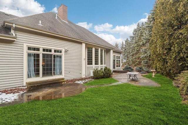 back of property with a patio, a lawn, a chimney, and roof with shingles