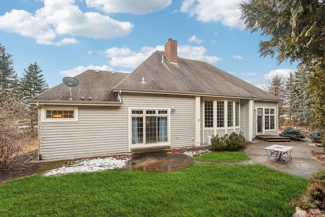 rear view of house featuring roof with shingles, a patio, a chimney, and a lawn