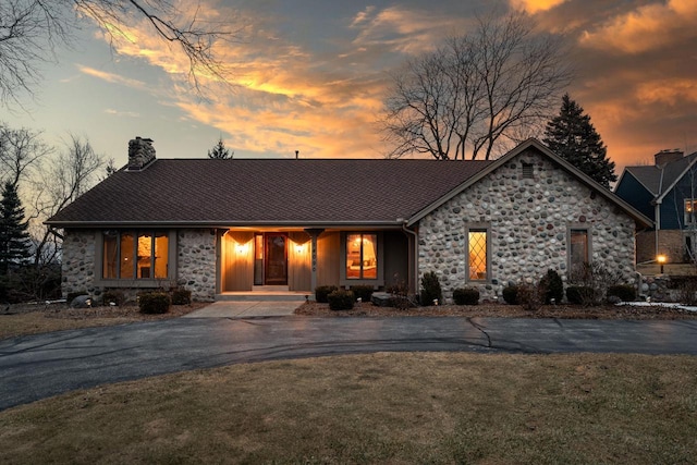 view of front of home featuring driveway, stone siding, a chimney, and a front yard