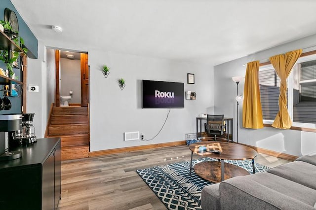 living room featuring stairs, light wood-type flooring, visible vents, and baseboards