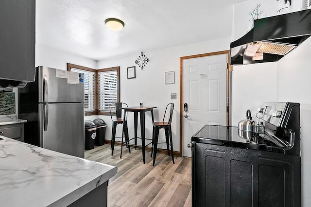 kitchen featuring electric stove, freestanding refrigerator, light stone countertops, light wood-type flooring, and exhaust hood