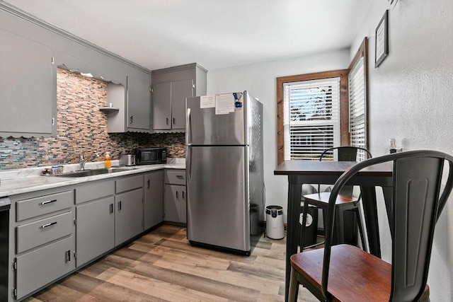 kitchen featuring a sink, light wood-type flooring, gray cabinets, freestanding refrigerator, and decorative backsplash