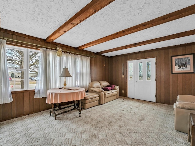 carpeted living room featuring a textured ceiling, wooden walls, and beamed ceiling