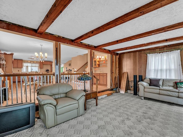 carpeted living area with plenty of natural light, a textured ceiling, beam ceiling, and a notable chandelier