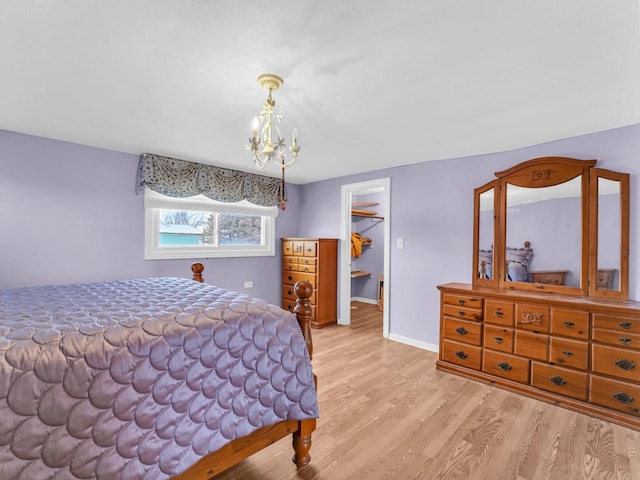 bedroom featuring light wood-style floors, a walk in closet, baseboards, and an inviting chandelier