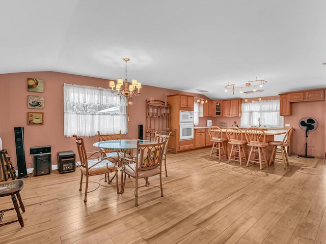 dining space featuring lofted ceiling, a notable chandelier, and light wood-style flooring