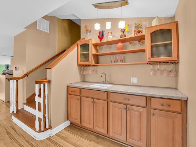 bar featuring visible vents, light wood-style floors, a sink, wet bar, and stairs