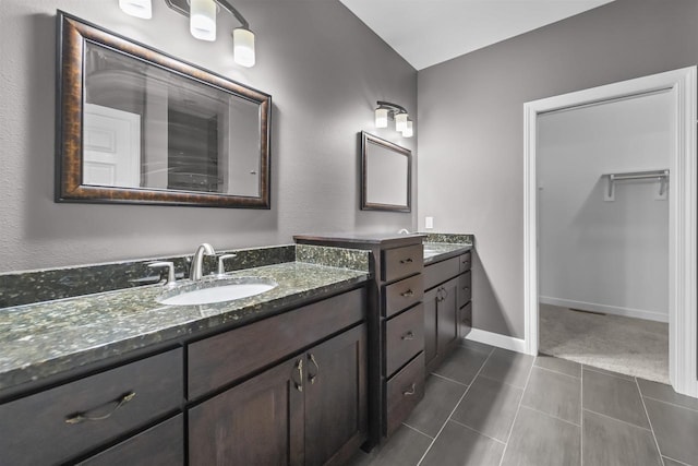 bathroom with two vanities, a sink, a walk in closet, and baseboards