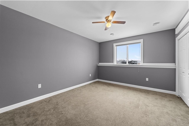 carpeted spare room featuring a ceiling fan and baseboards