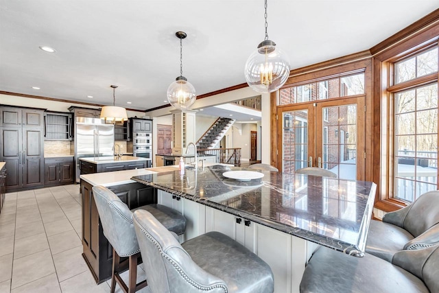 kitchen with a breakfast bar area, light tile patterned floors, appliances with stainless steel finishes, ornamental molding, and a large island with sink