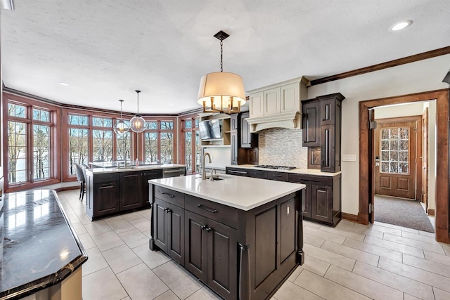 kitchen featuring a kitchen island with sink, light countertops, tasteful backsplash, decorative light fixtures, and stainless steel gas stovetop