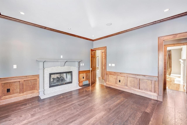 unfurnished living room with a wainscoted wall, recessed lighting, a tiled fireplace, and wood finished floors