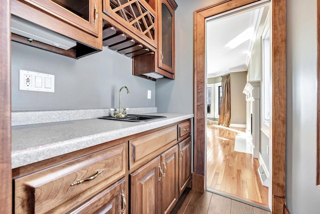 kitchen with light wood finished floors, glass insert cabinets, ornamental molding, light countertops, and a sink