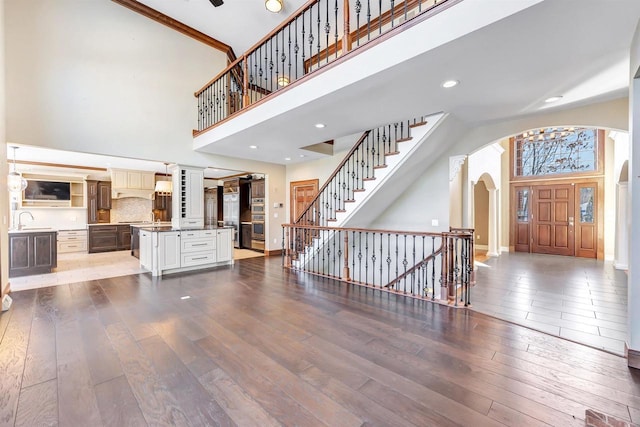 living area with arched walkways, a high ceiling, baseboards, and hardwood / wood-style flooring