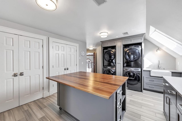 kitchen with a sink, visible vents, wood counters, gray cabinets, and stacked washer and clothes dryer