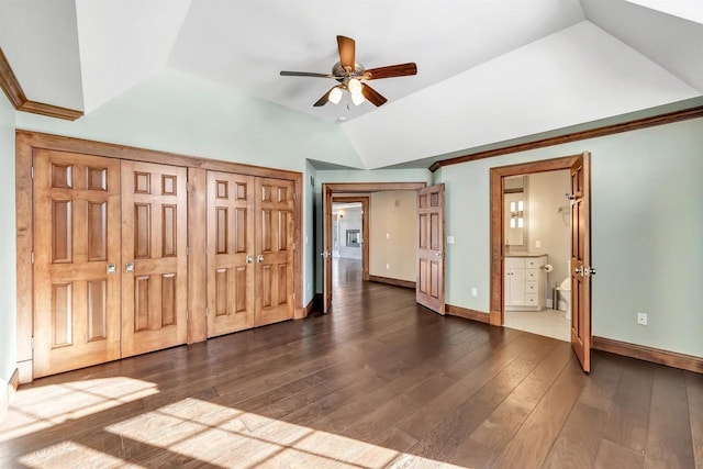 unfurnished bedroom with dark wood-style floors, lofted ceiling, ensuite bathroom, ornamental molding, and baseboards