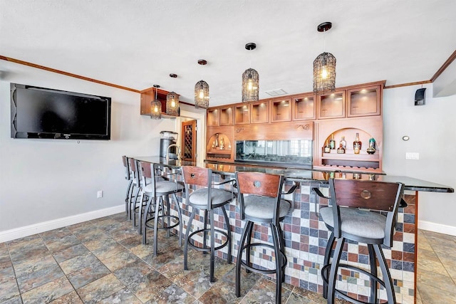 kitchen featuring a breakfast bar, pendant lighting, brown cabinetry, glass insert cabinets, and baseboards