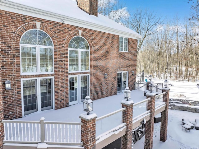 snow covered property with brick siding and a chimney