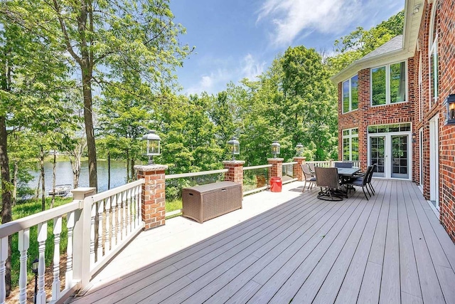 deck with outdoor dining space, french doors, and a water view