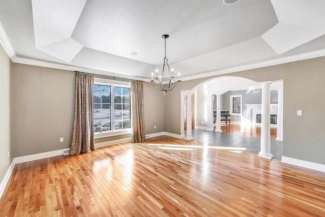 unfurnished dining area with a fireplace, baseboards, light wood-style floors, a raised ceiling, and decorative columns