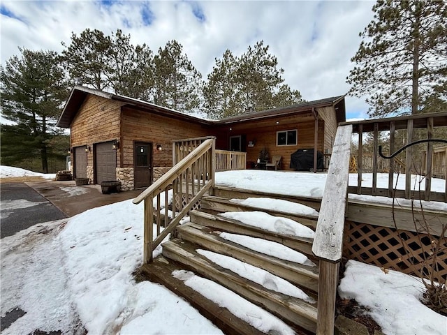 snow covered property with driveway, a wooden deck, an attached garage, and stairs