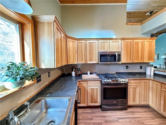 kitchen featuring light brown cabinets, stainless steel appliances, a sink, light wood-style floors, and dark countertops