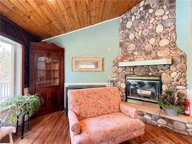 living area with lofted ceiling, a stone fireplace, wooden ceiling, and wood finished floors