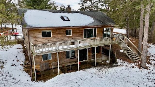 snow covered rear of property featuring a chimney, stairway, and a deck