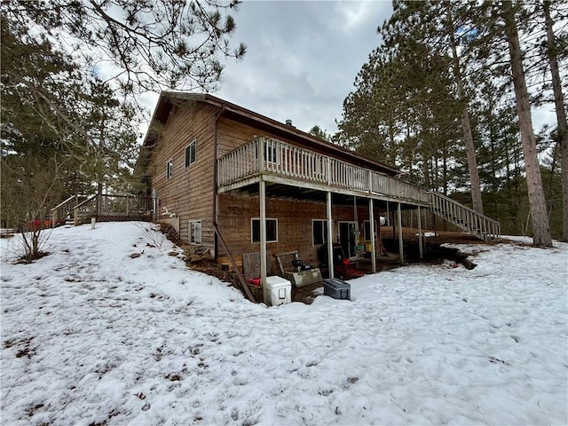 snow covered back of property featuring stairs and a wooden deck