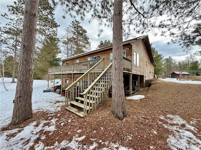 snow covered house with a deck, stairway, and a chimney