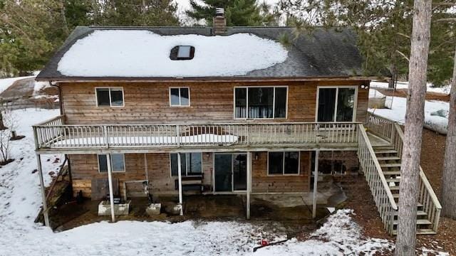 snow covered rear of property featuring a patio area, stairway, a chimney, and a wooden deck